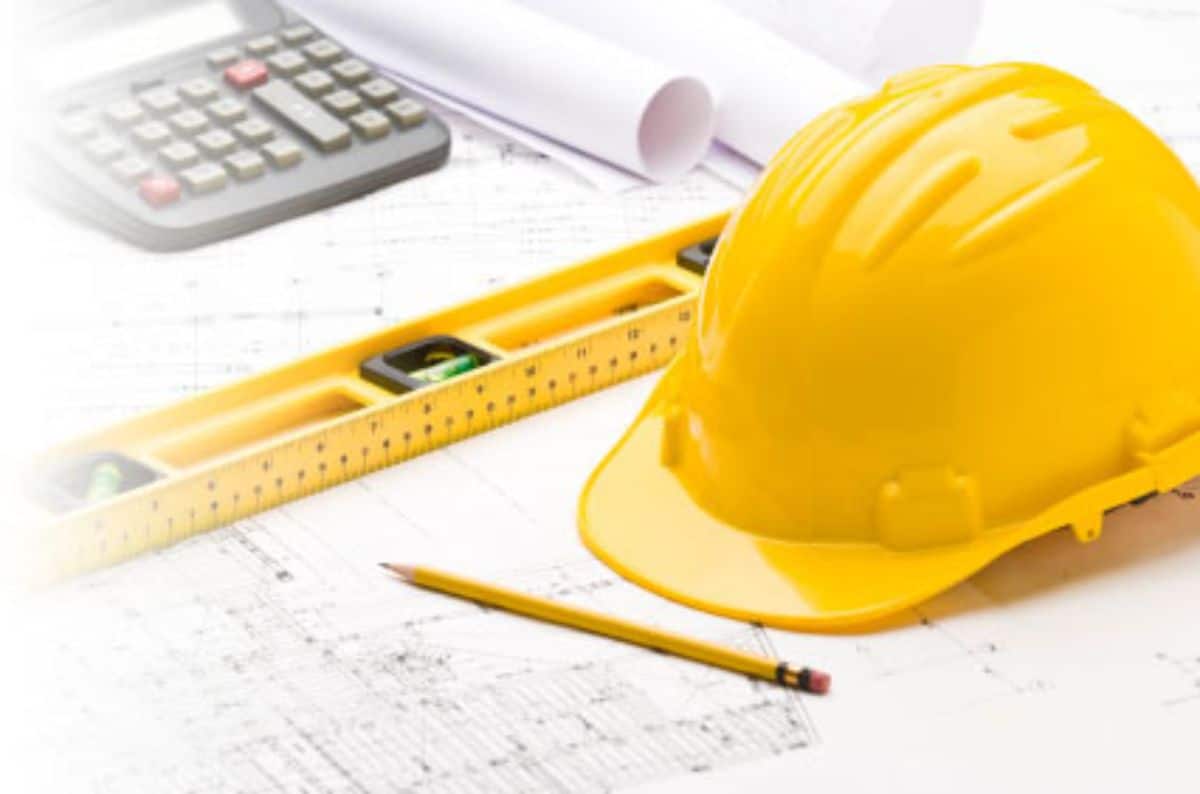 yellow hardhat on a desk with calculator and floor plans
