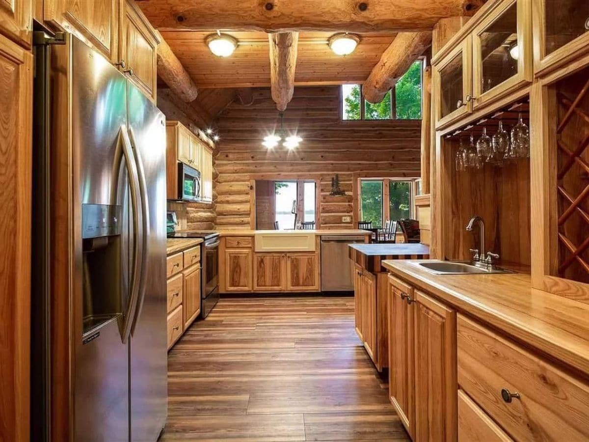 view down length of kitchen with refrigerator on left foreground and wine cabinet on right