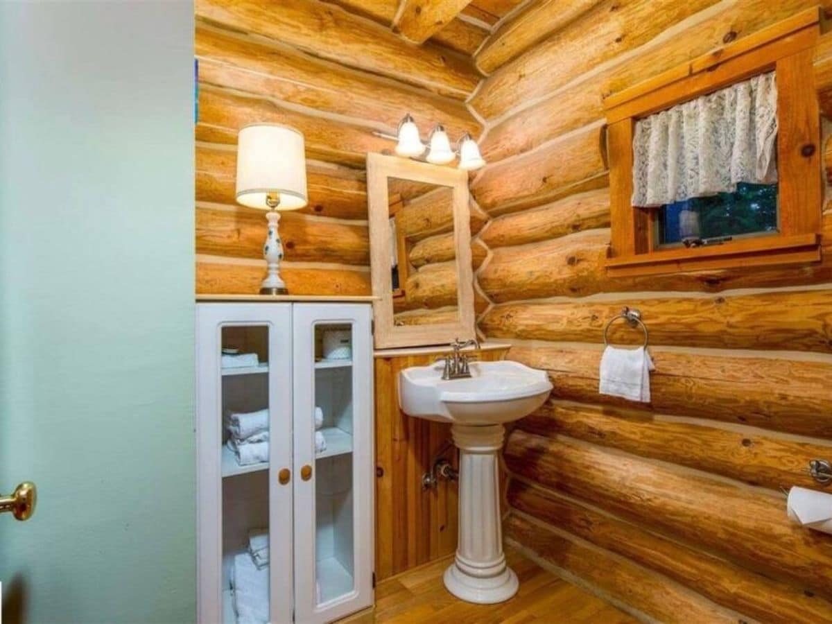 white pedastal sink against wall in log cabin bathroom