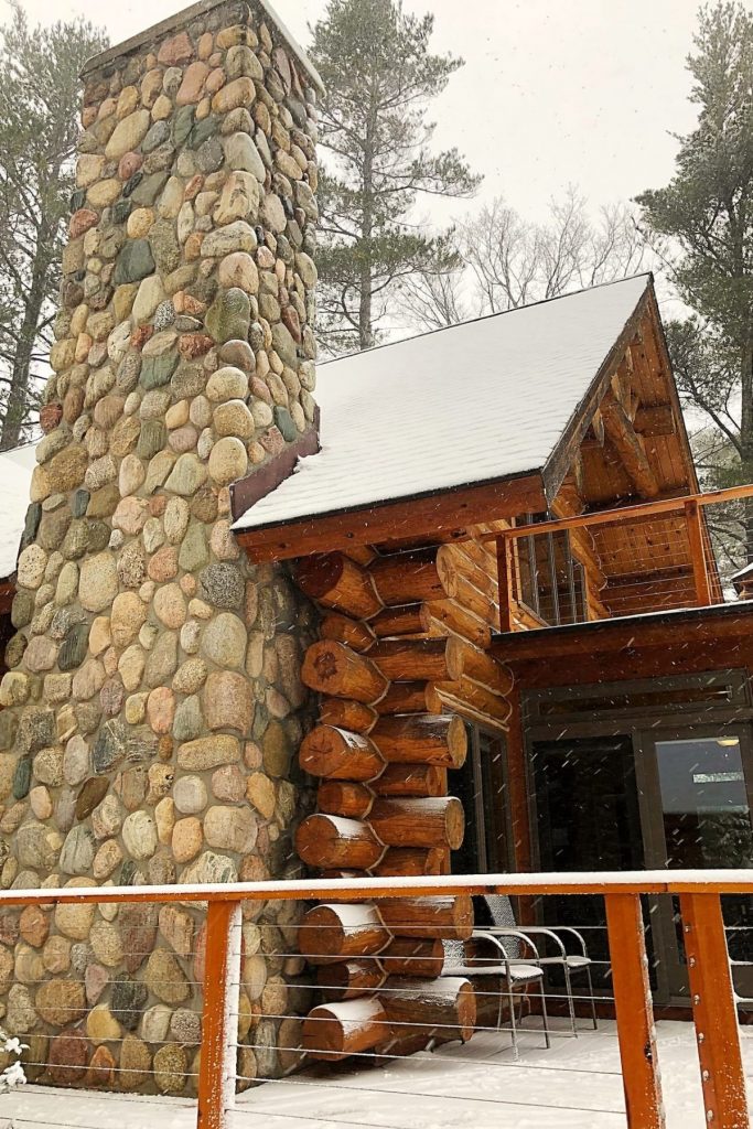 stone fireplace on side of log cabin in winter