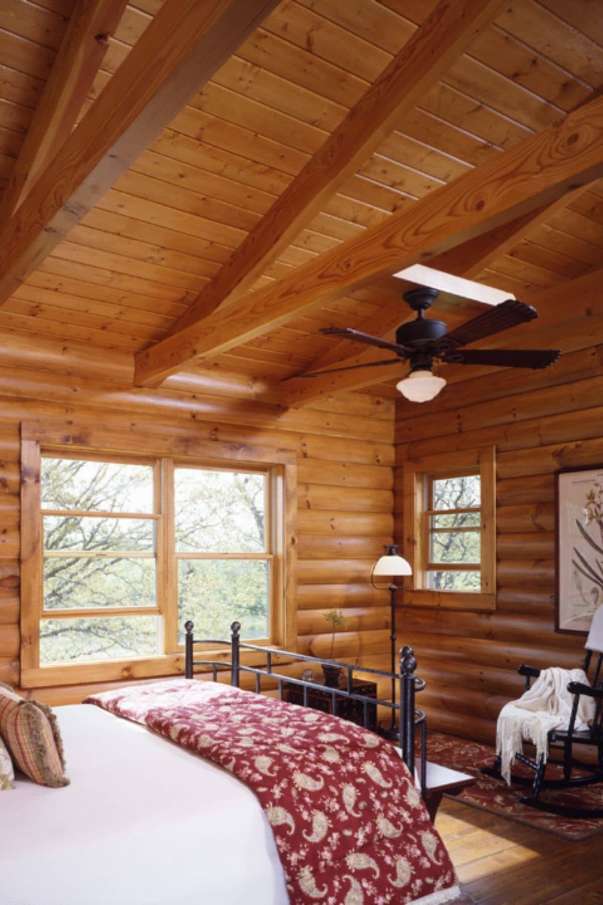 bed with red blanket in log cabin with large window on side