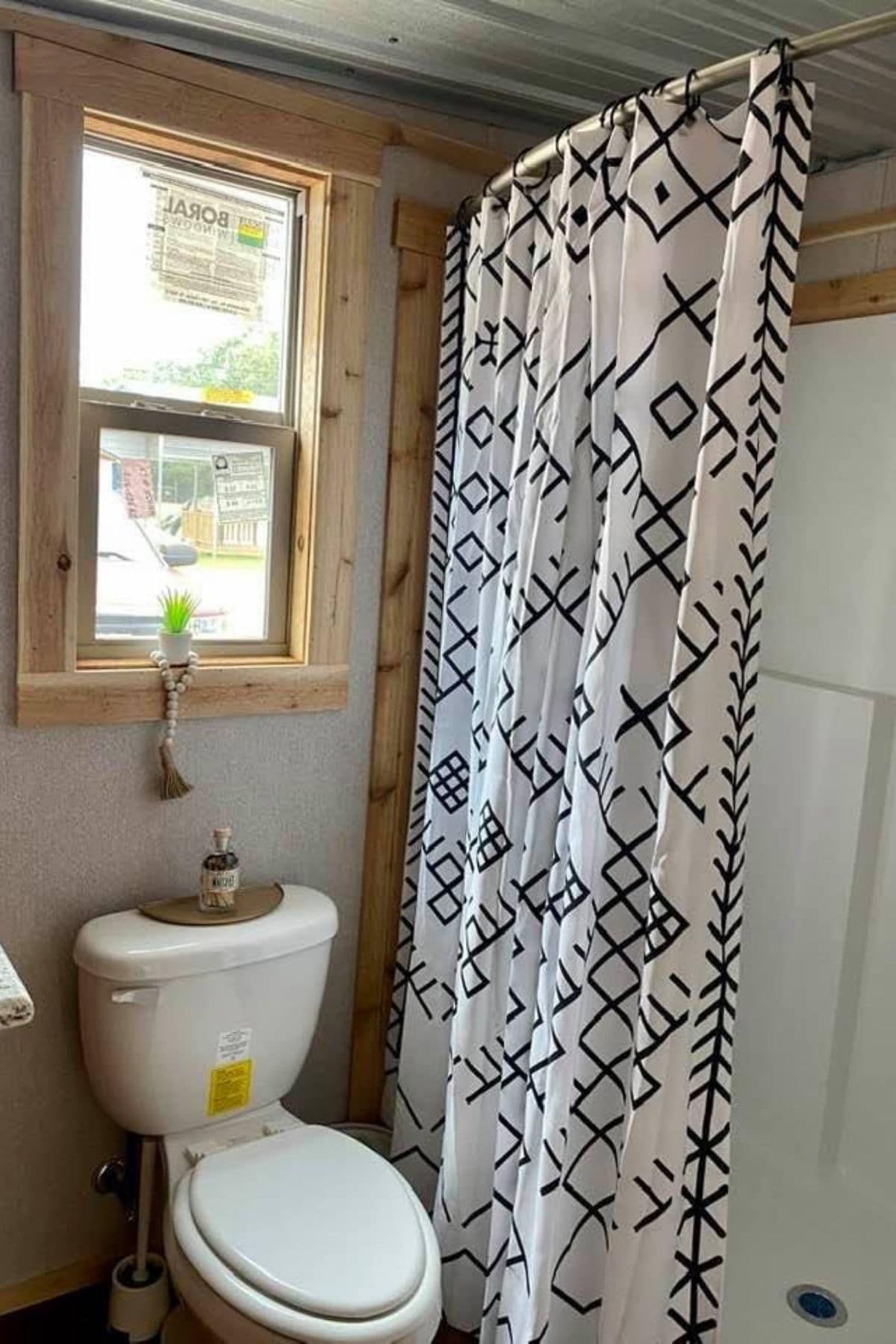 flush toilet next to shower stall under window with wood trim
