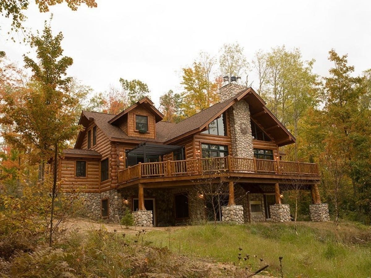 log home with rock blocks under balcony against woods