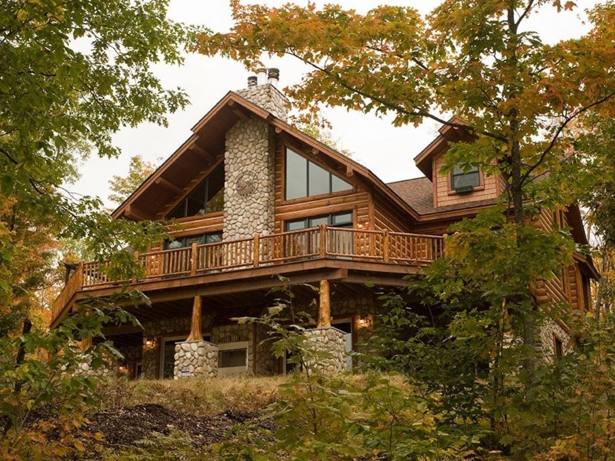 back of log home with rock chimney and elevated balcony over basement entrance