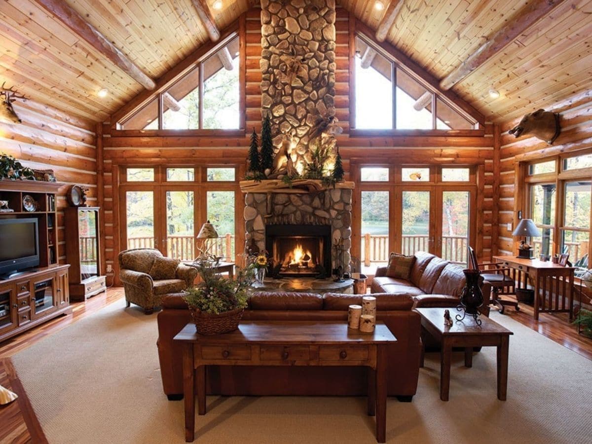 living room inside log cabin with rock fireplace between large windows