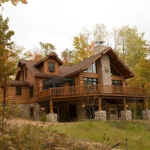 log home with rock blocks under balcony against woods
