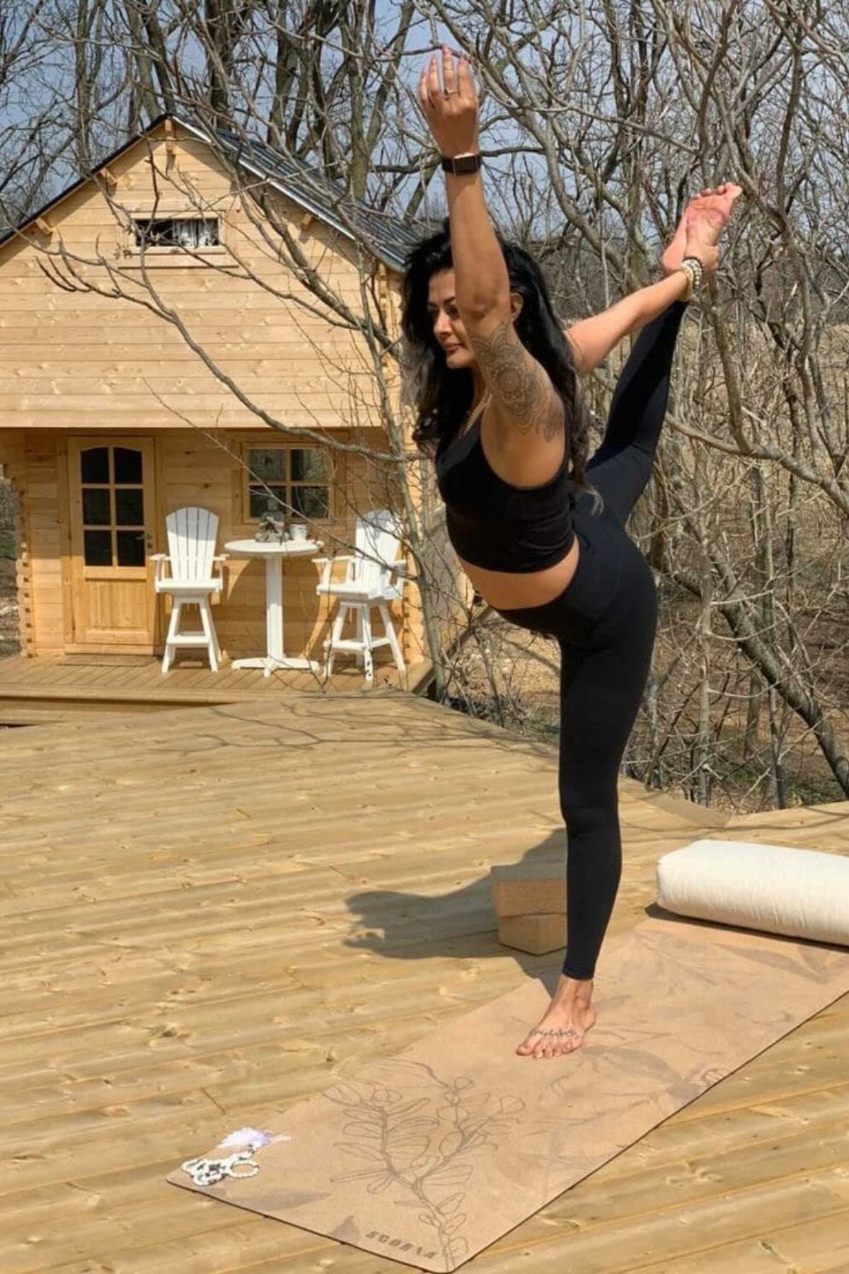 woman in black stretching in front of tiny log home