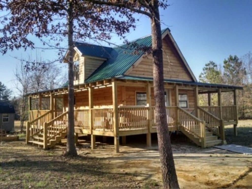 light wood log cabin with wrap porch and green roof