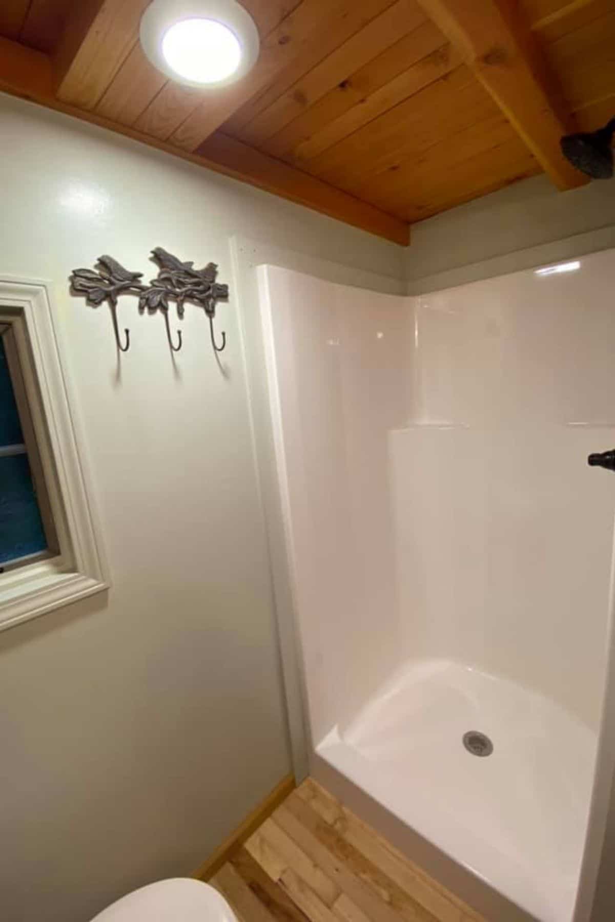 open white shower stall with metal hooks on wall between shower and window