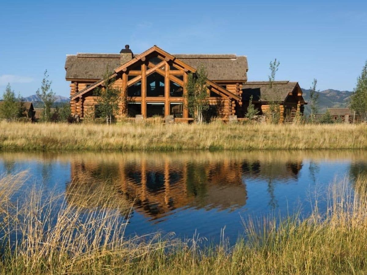 log cabin by pond with grass in foreground