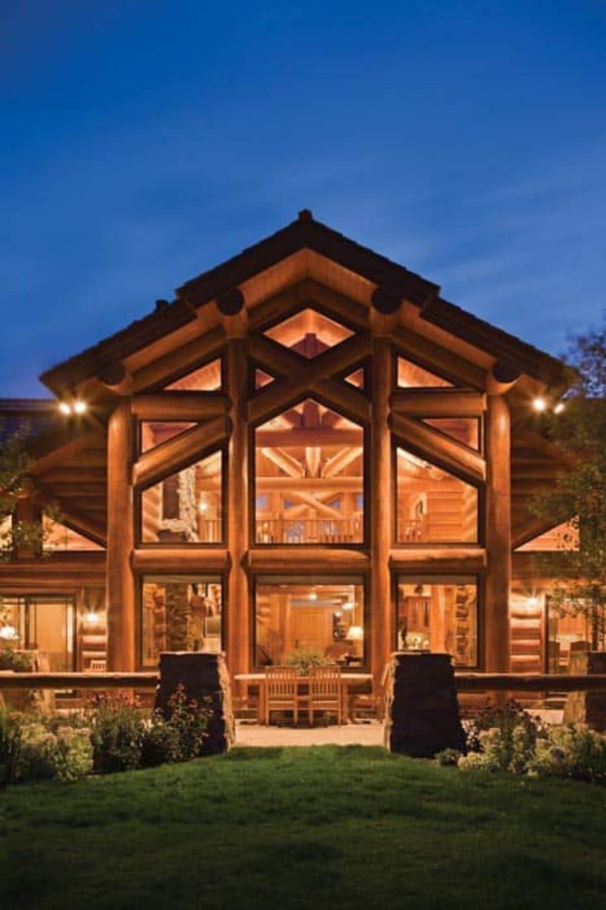 log cabin great room lit up after dark pictured from outside against blue sky