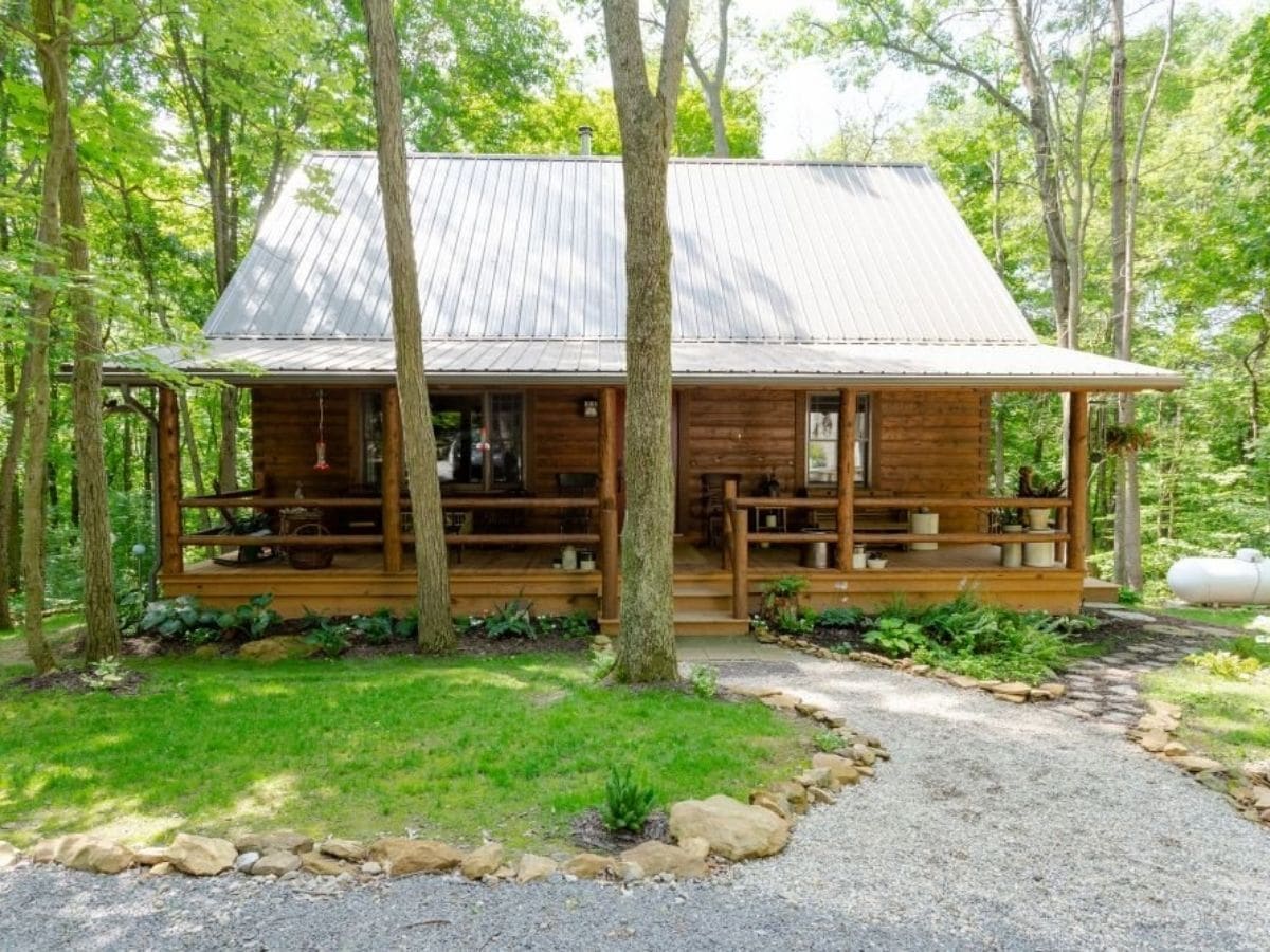 log cabin with large porch behind trees