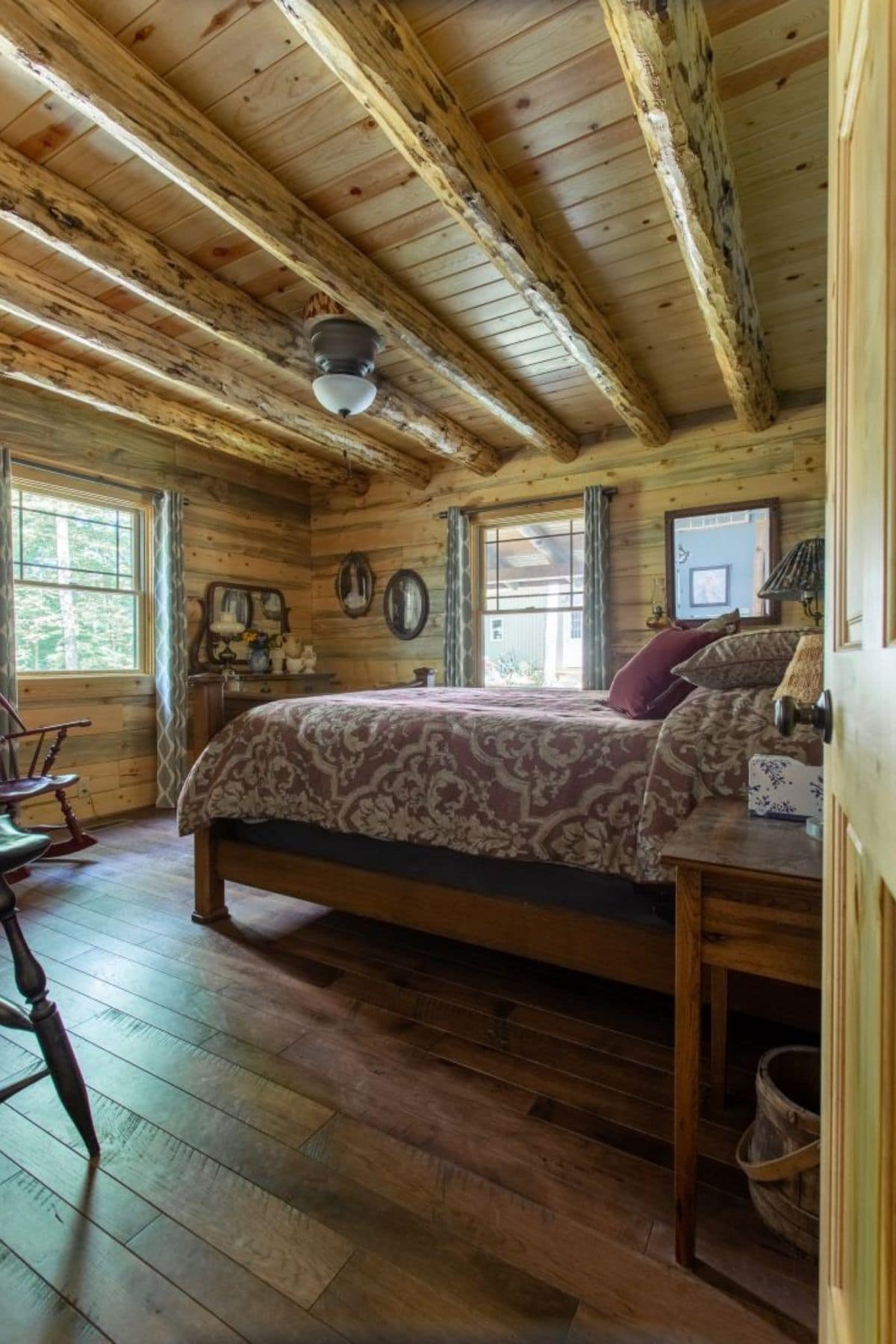 bed against right wall with windows on all walls in log cabin