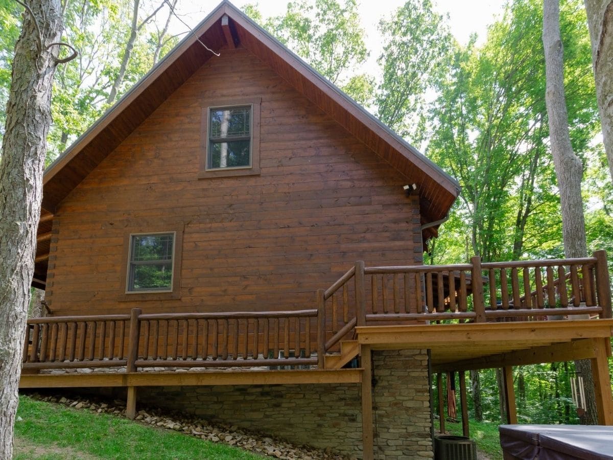 side of log cabin with walk around porch and two windows