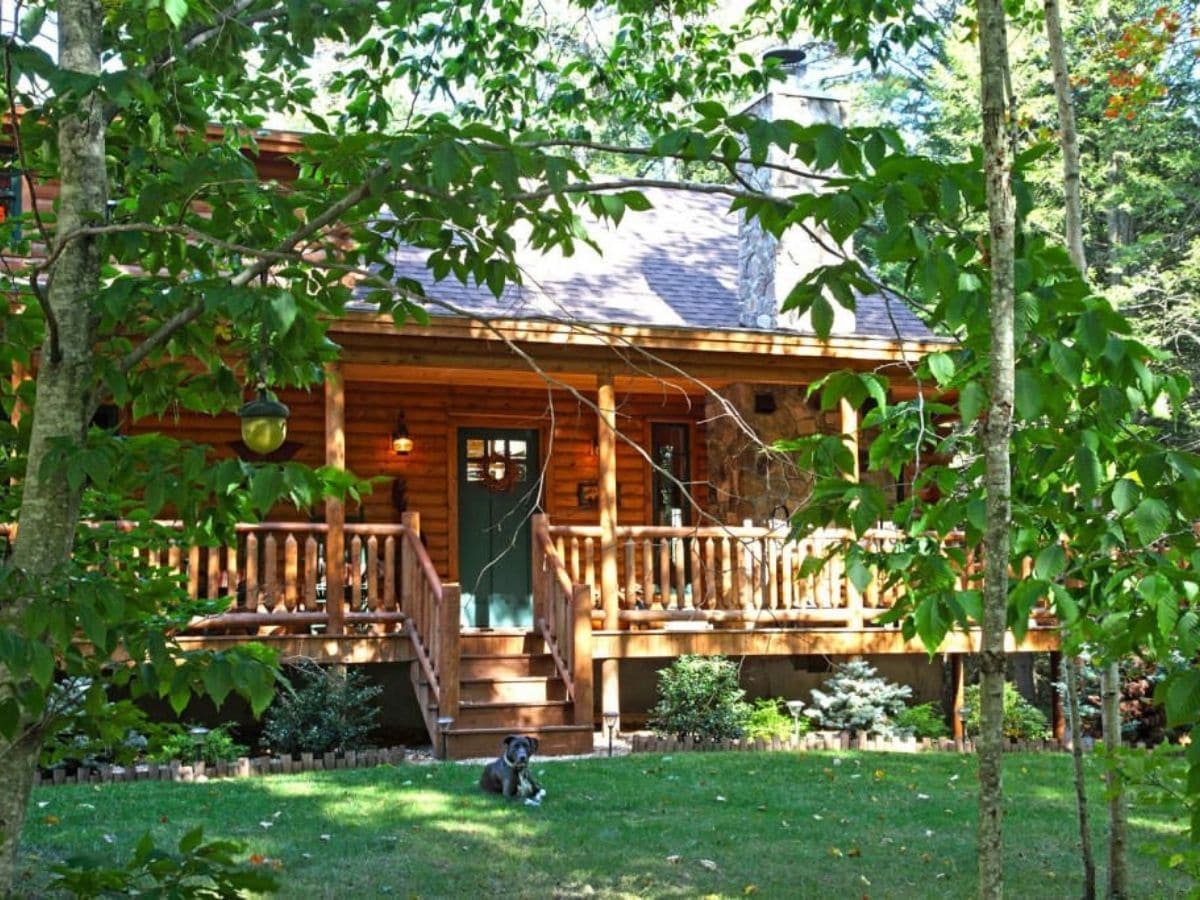 front of log cabin porch with trees in front of home