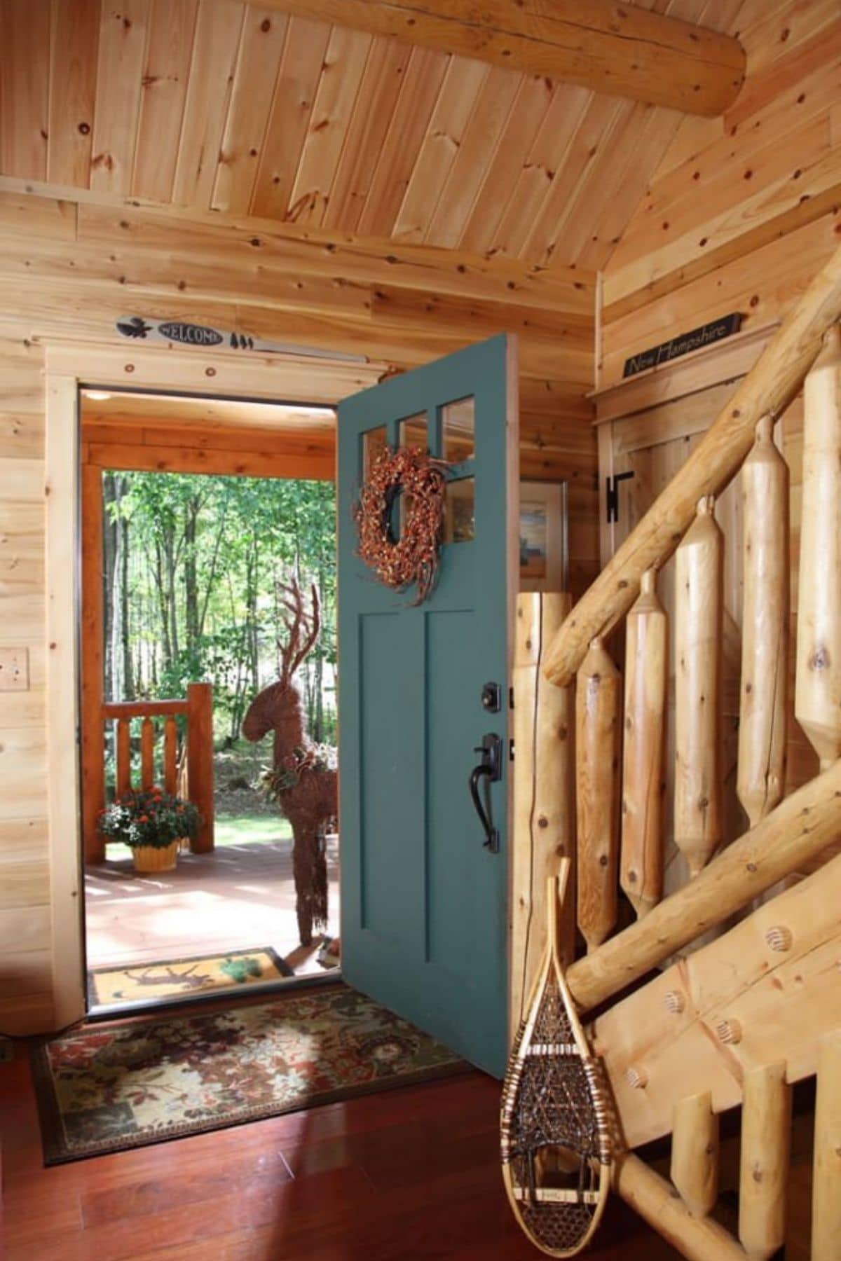 open blue front door from inside showing log walls and railing on staircase