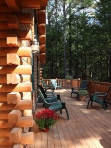 corner of log cabin with notched logs by porch with green chairs