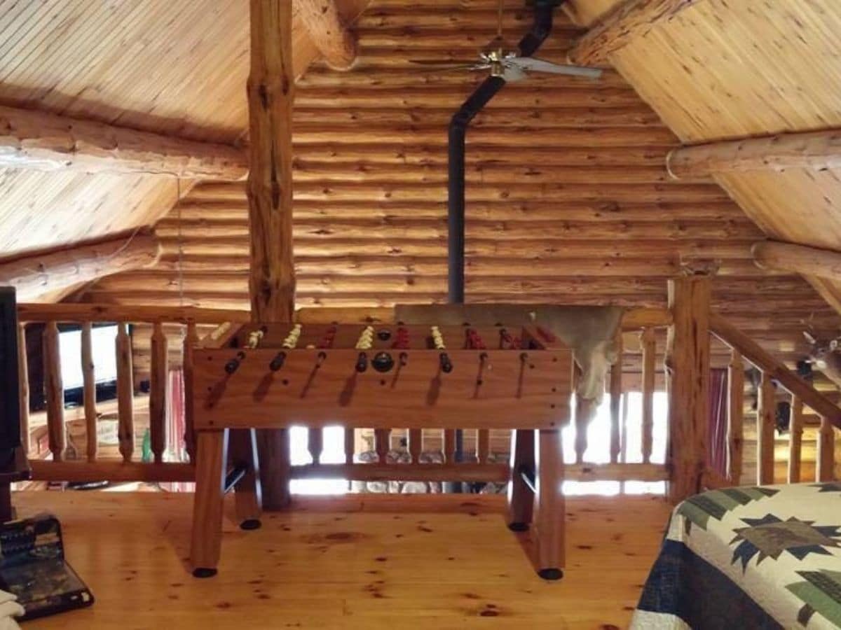 foosball table at edge of loft railing with log cabin background wall