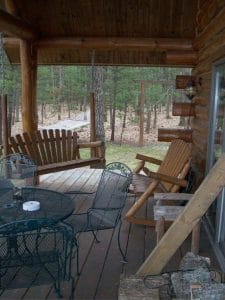 porch with rocking chairs and metal table in front of log cabin