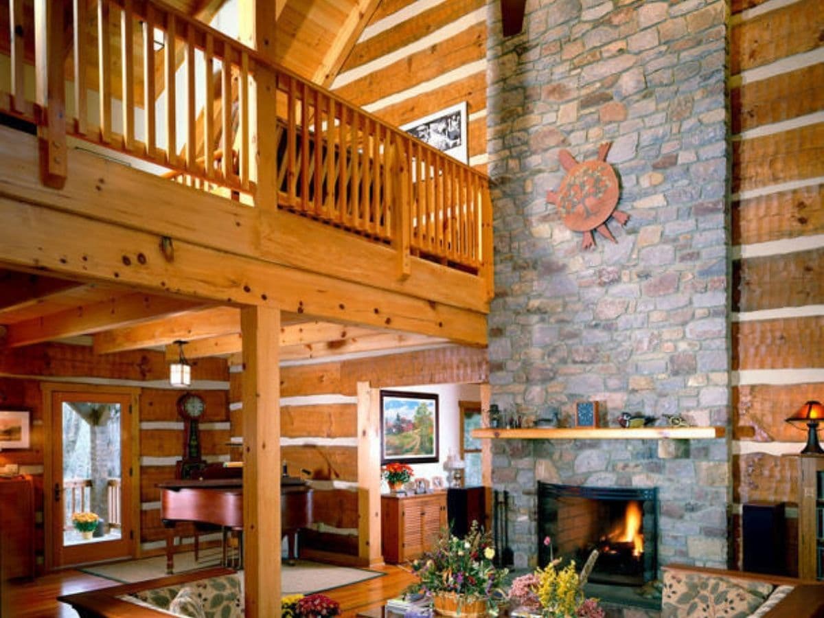 stone fireplace against log cabin walls with loft railing on top left