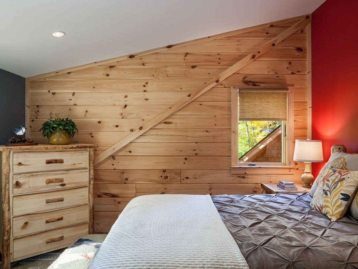 bed against red wall with angled wood roofline and white bedding