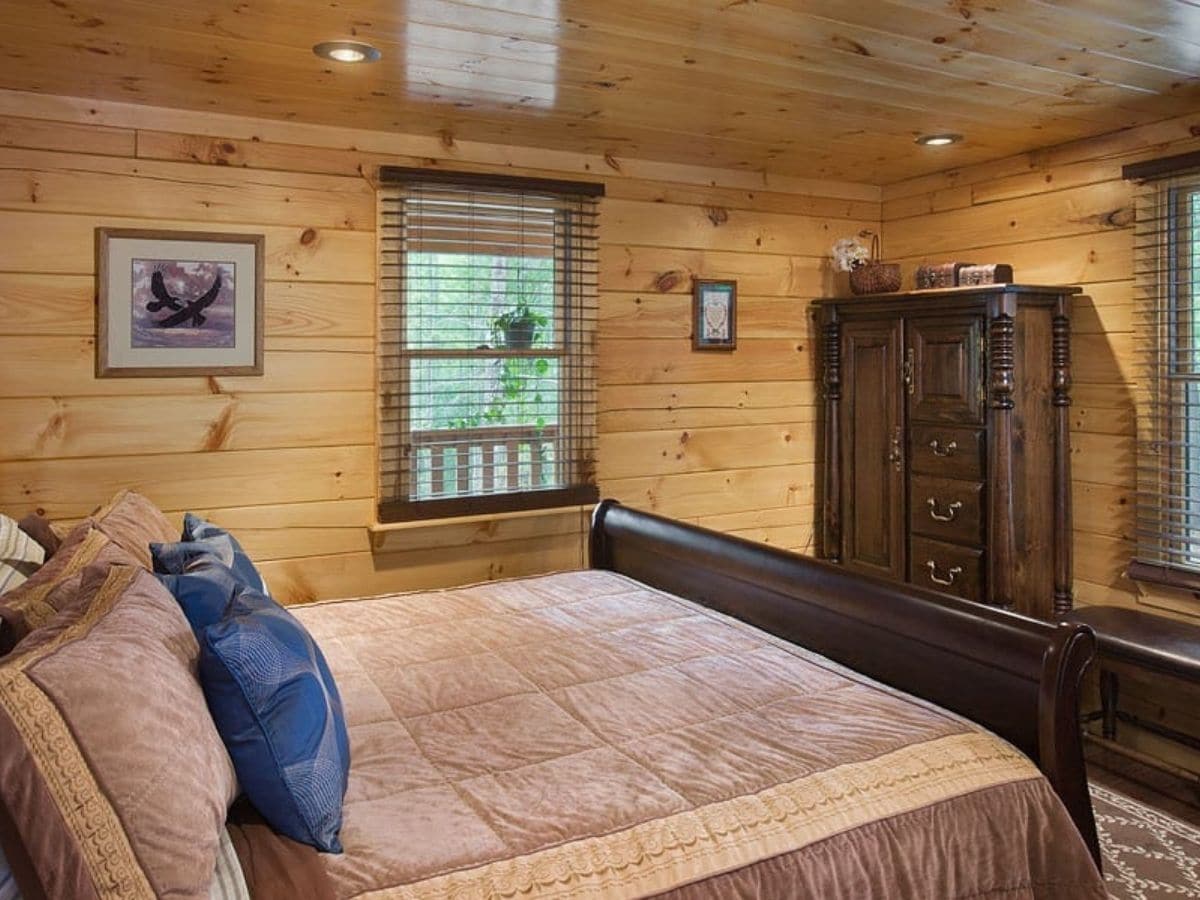 wood bedframe in log cabin bedroom with window on wall