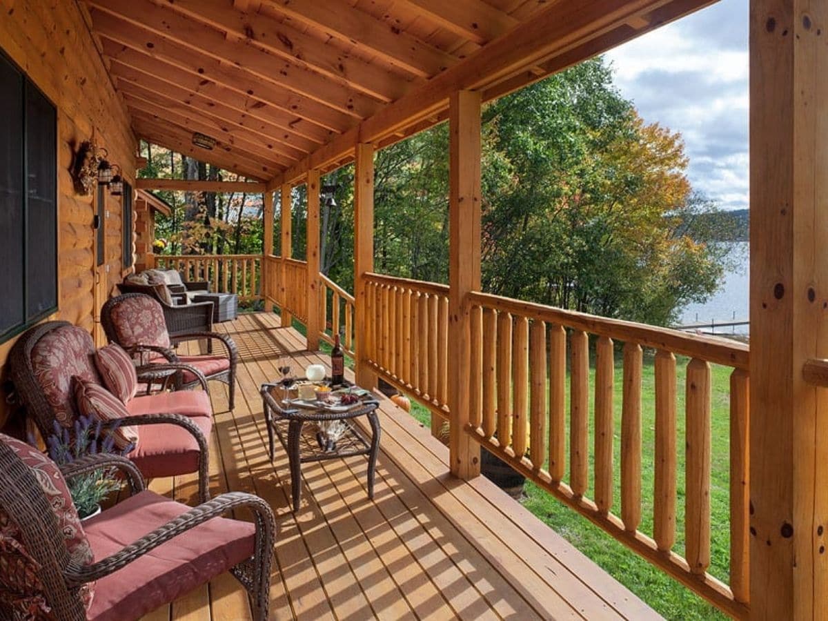 front porch on cabin with wood railing and red chairs and open table