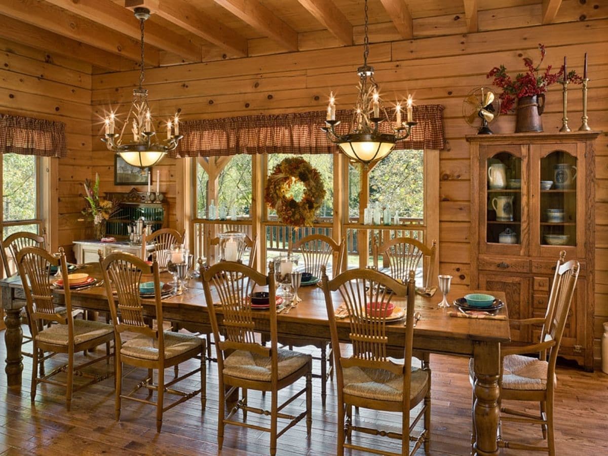 classic wood dining table with chandeliers above in log cabin