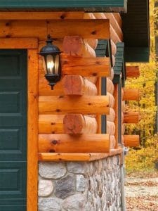 corner of log cabin with green door on left and stone below log on right