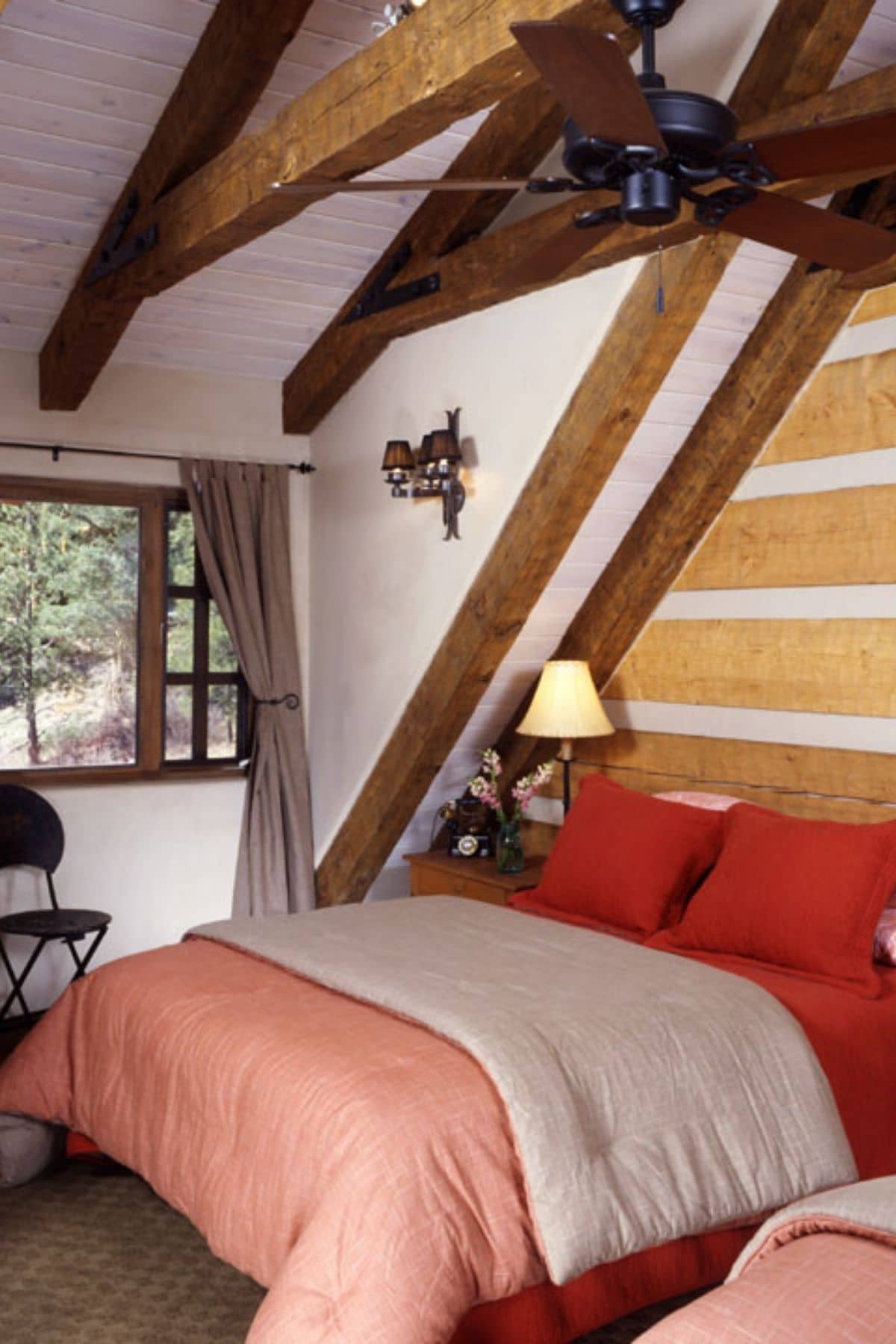 Bed against log cabin wall with pink and red bedding