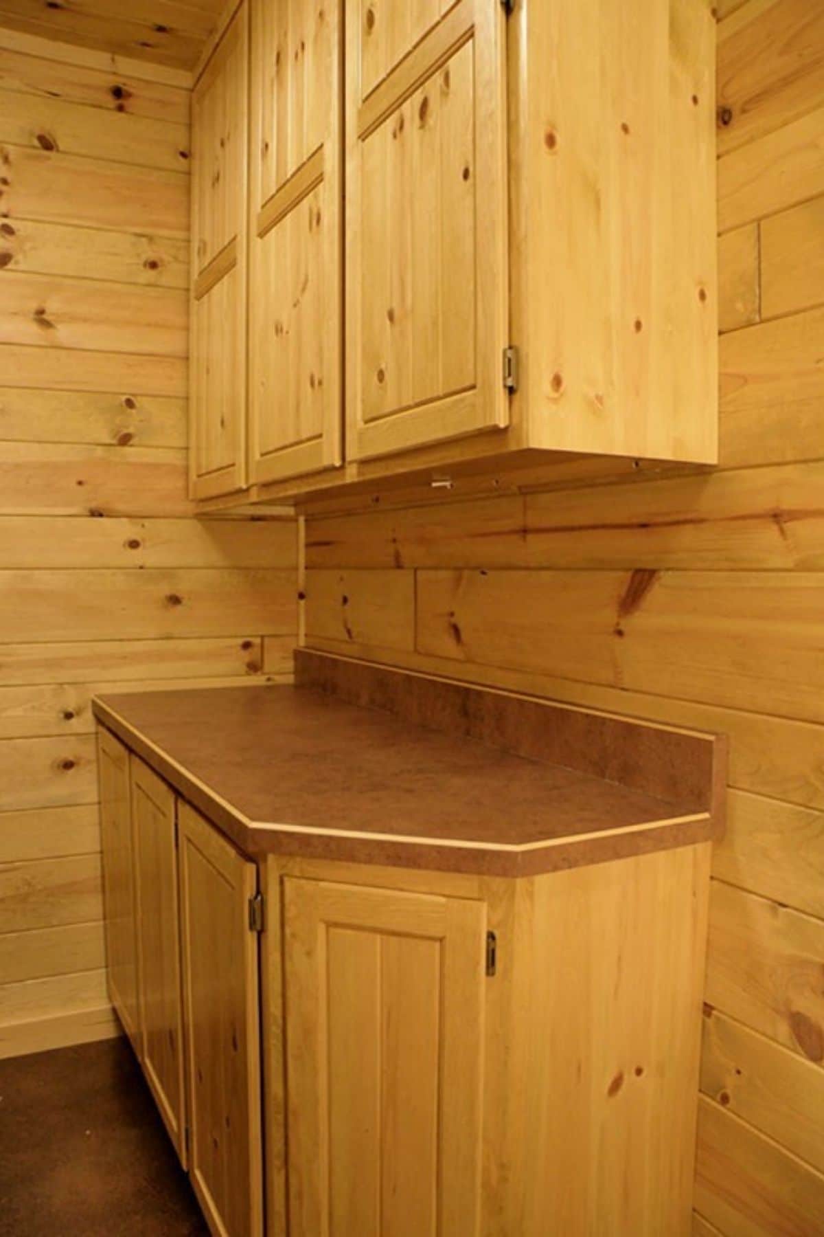 corner cabinet in log cabin with dark wood countertop and light wood cabinets on wall