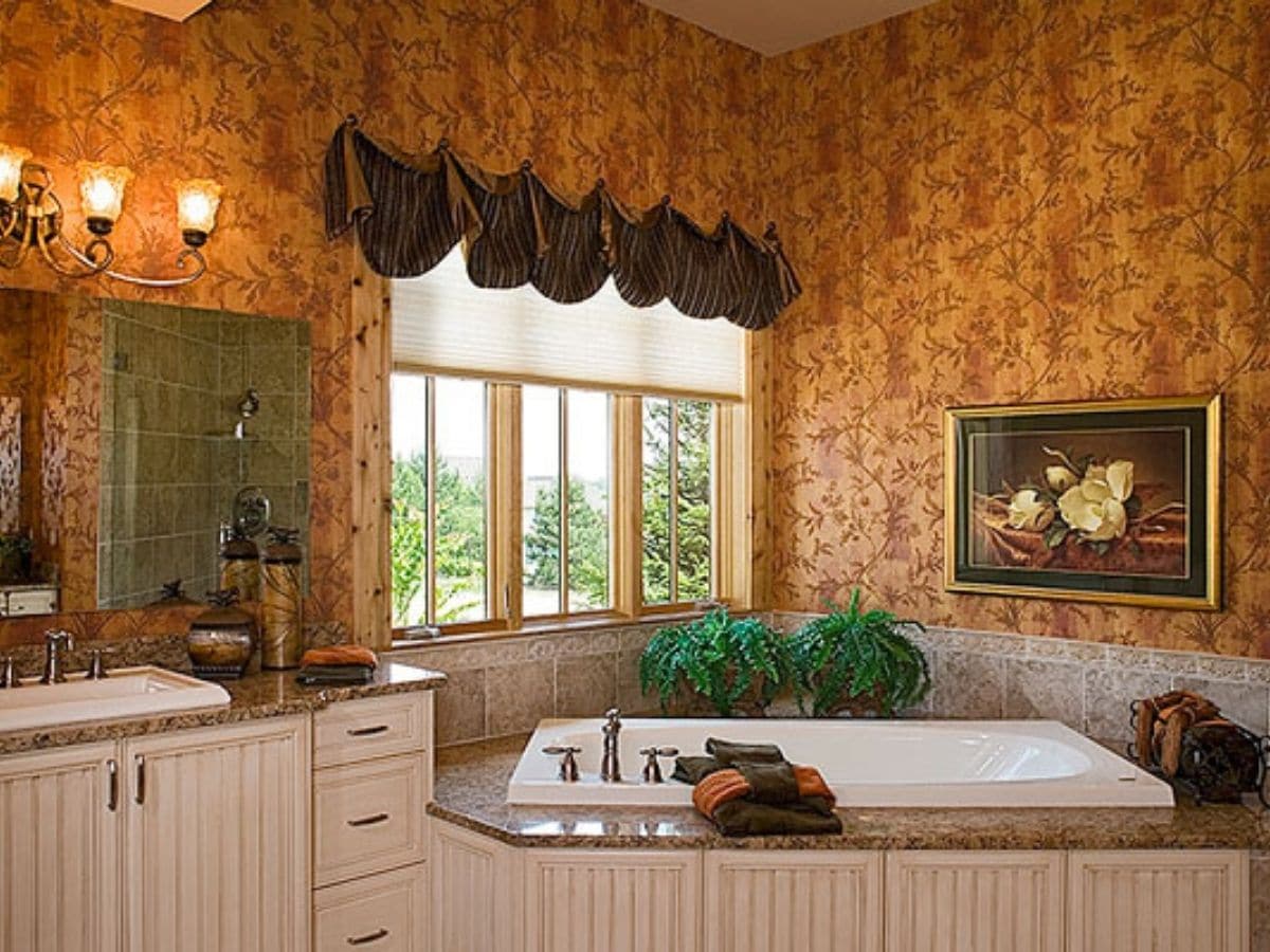 white sokaing tub in white washed wood cabinetry underneath window with floral wallpaper