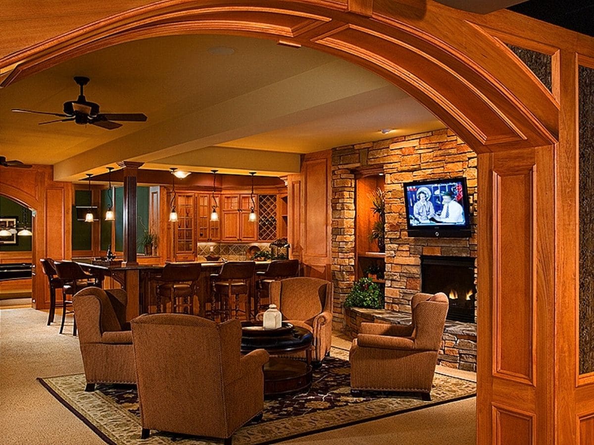 basement game room with arch entry and television mounted above stone fireplace on right