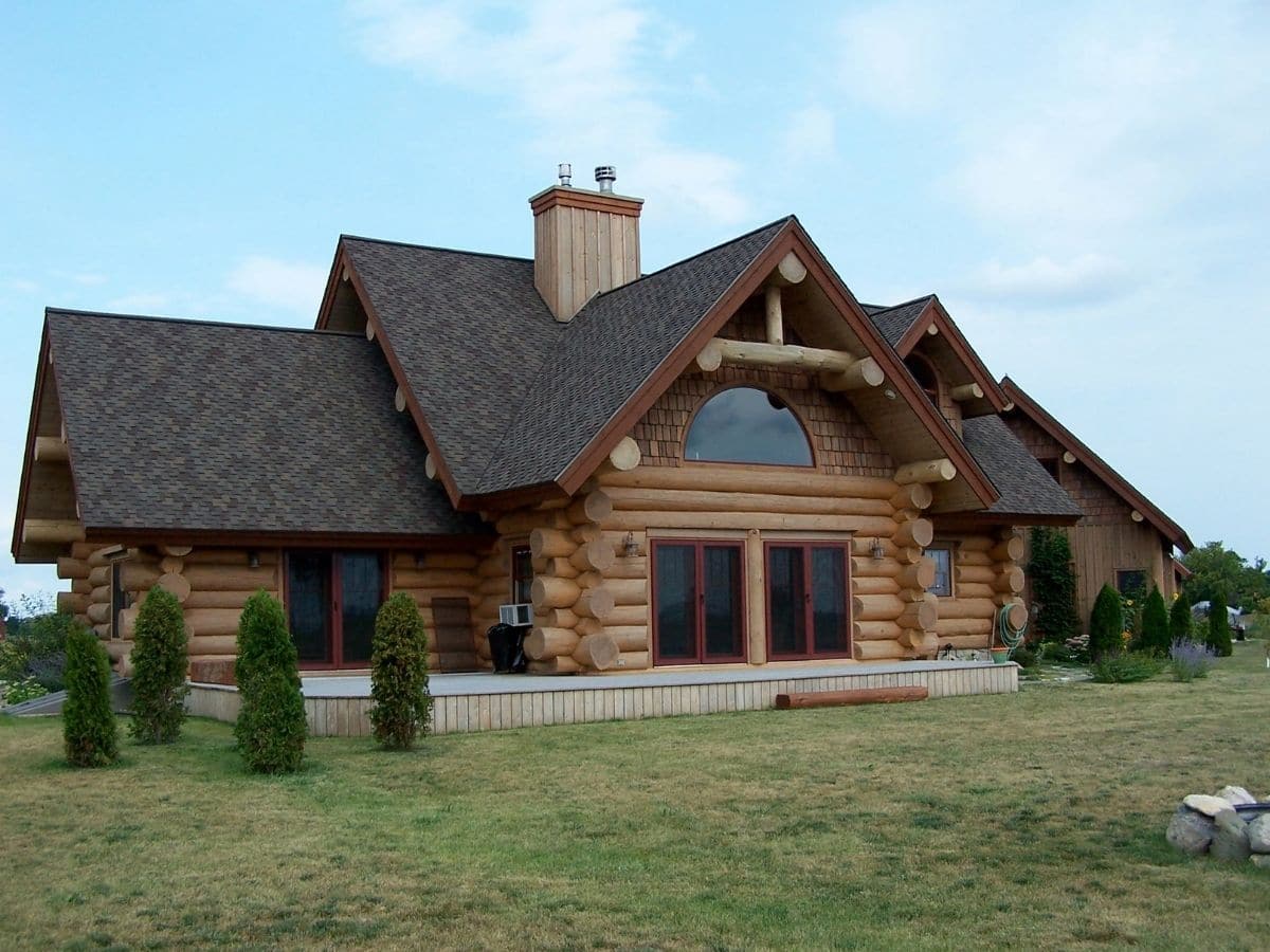 front of log home with shingle roof and shrubs outside