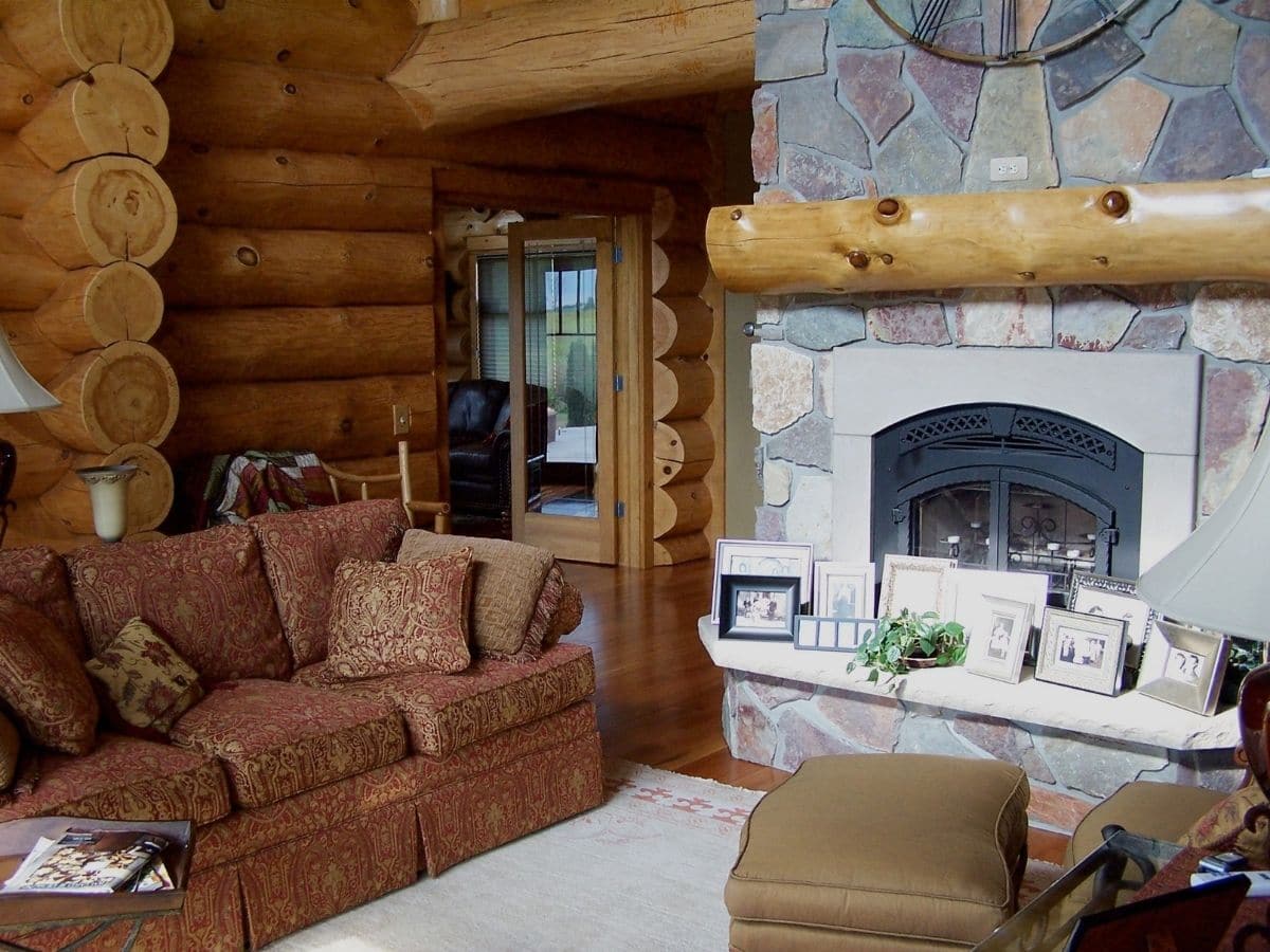 stone fireplace against wall with brown sofa in front and opening to kitchen on back left