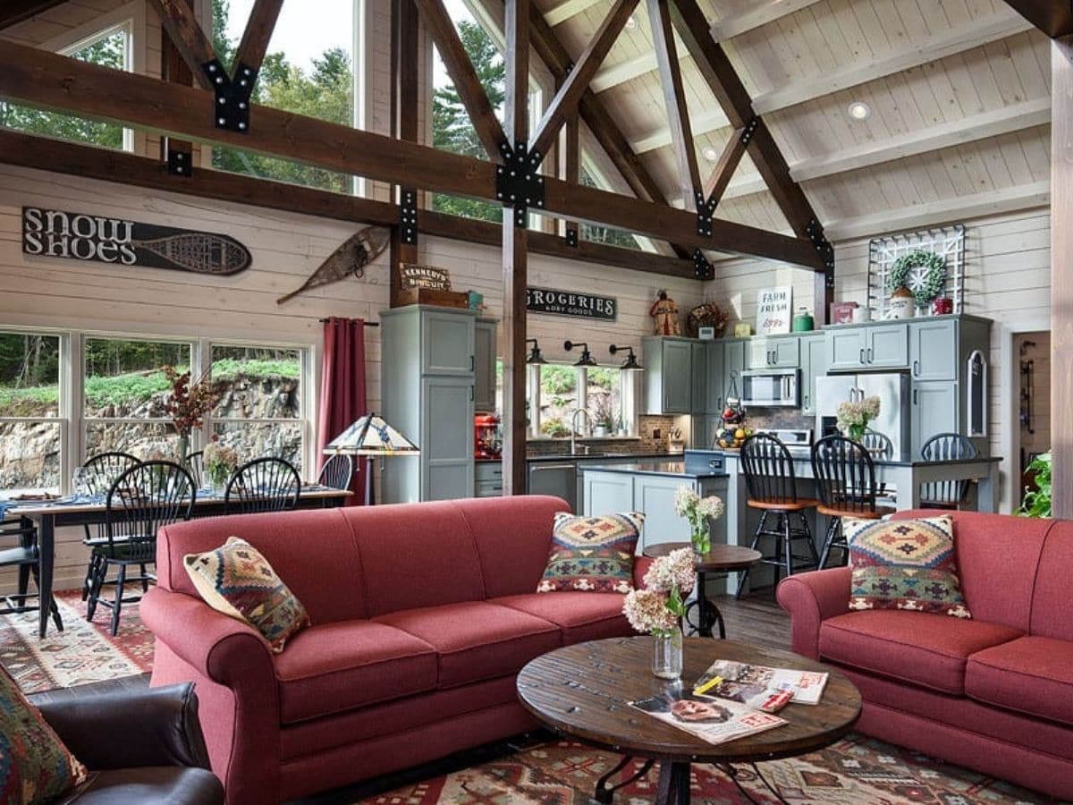 two maroon sofas with round table in open great room of log cabin with gray wood walls