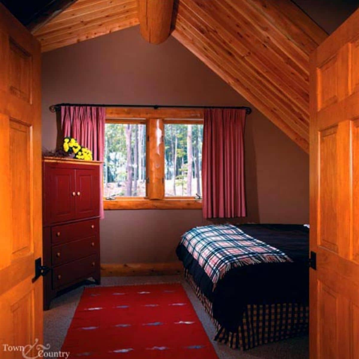 view into bedroom with red rug on floor and bed to right with dresser to left