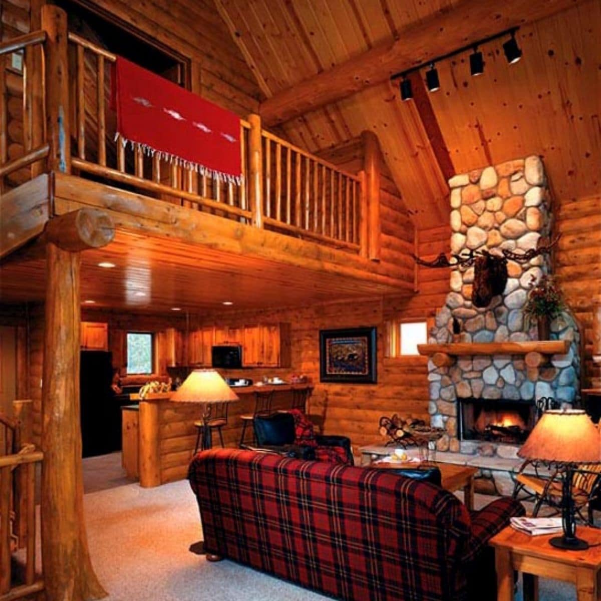 red plaid sofa in foreground of room with stone fireplace in back and loft above to right