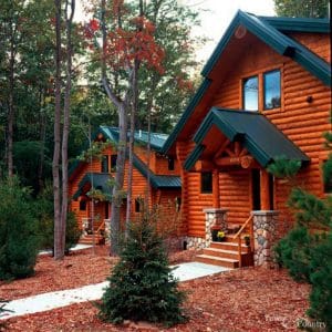 dark wood log cabin with green roof and white walkway