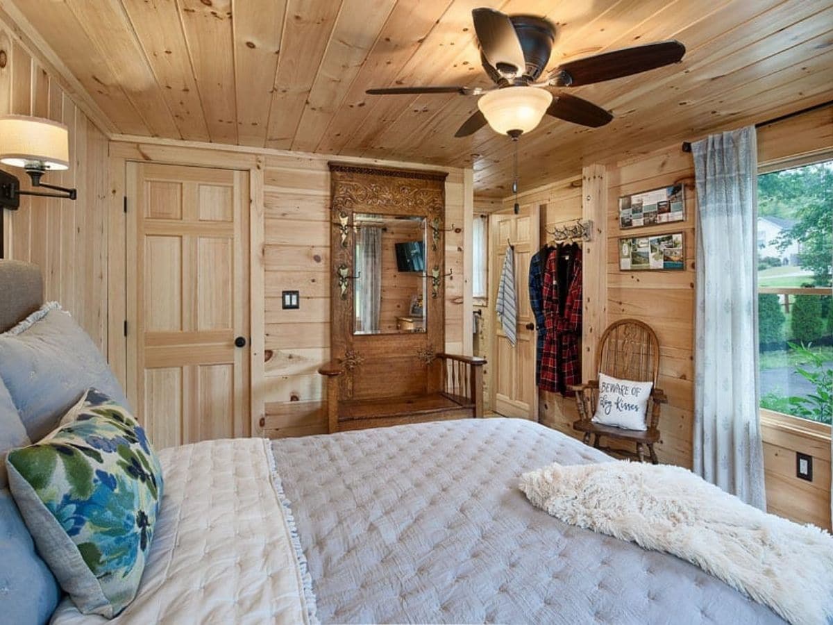 white bedding in log cabin bedroom with ceiling fan above bed