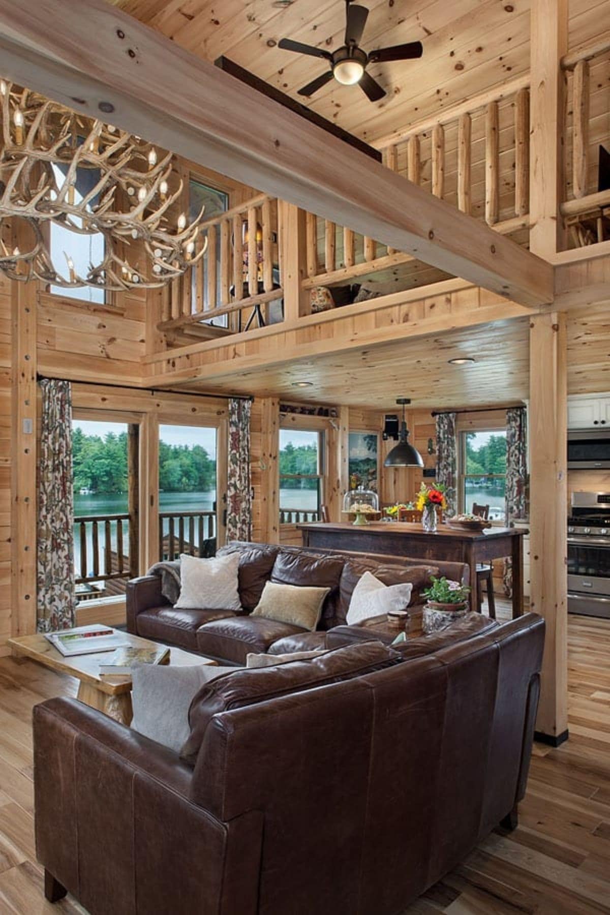 brown leather sofas beside each other under antler chandelier with loft railing above in background