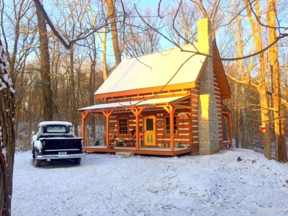 small log cabin in snow with old black truck in front