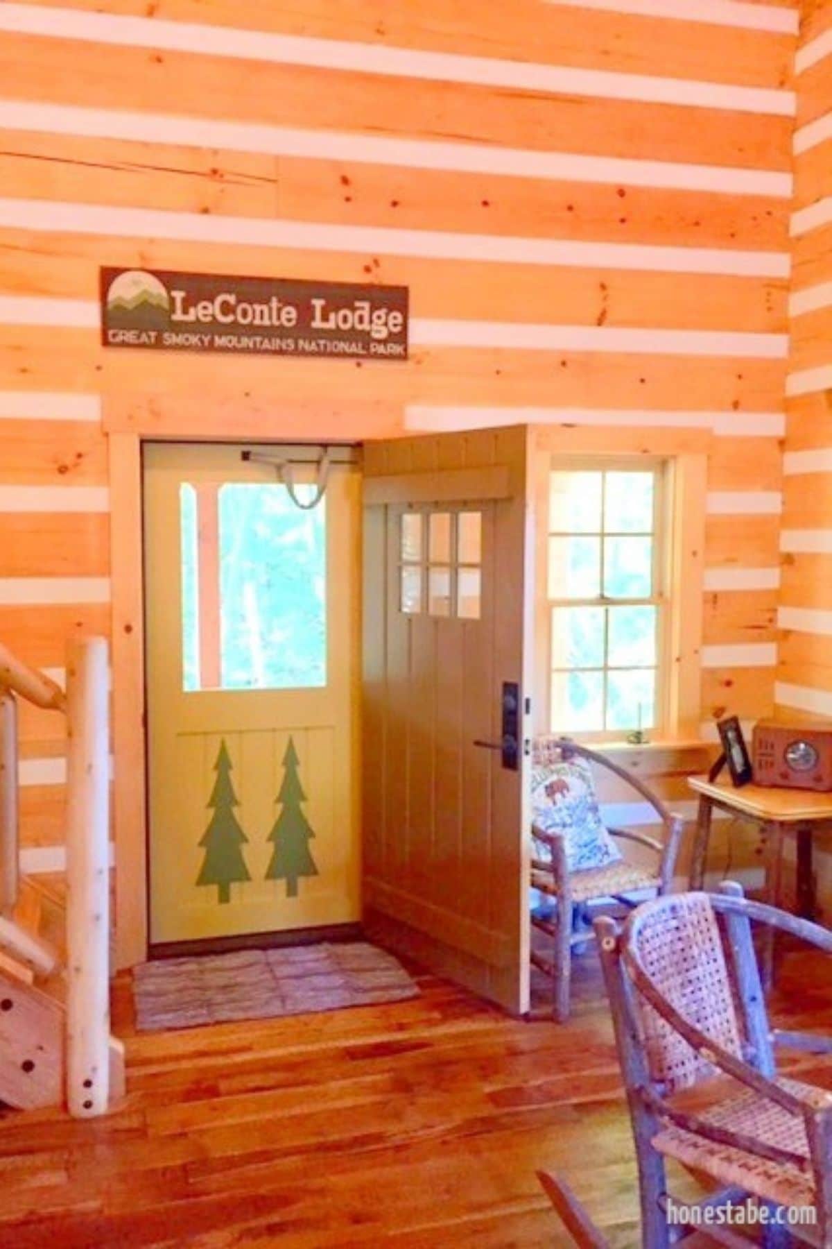 inside front door of log cabin with yellow door that is painted with green trees