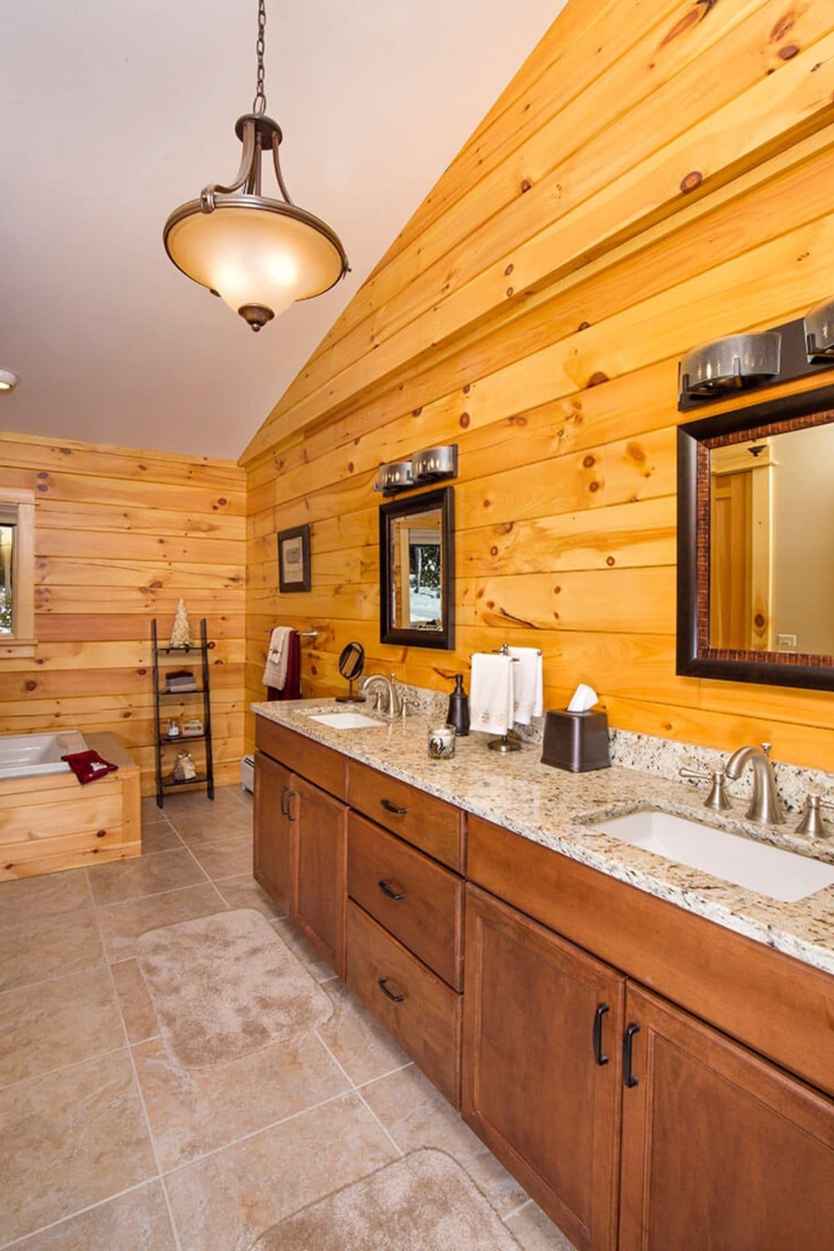 vanity with dark wood cabinets and two sinks against right wall of bathroom with wood surrounding bathtub at back end of room and log walls