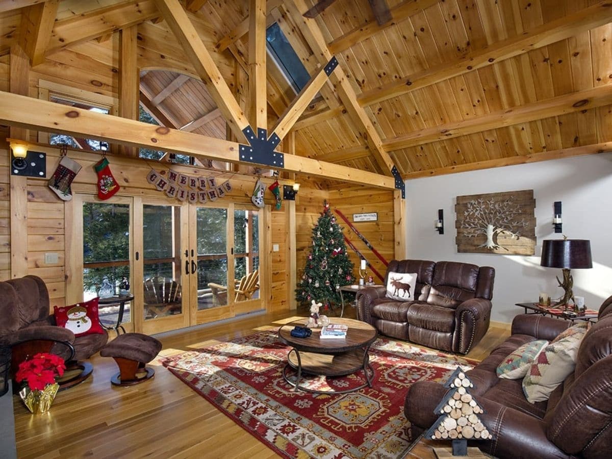 living room with maroon rug on floor christmas tree on side wall and brown sofa against white wall