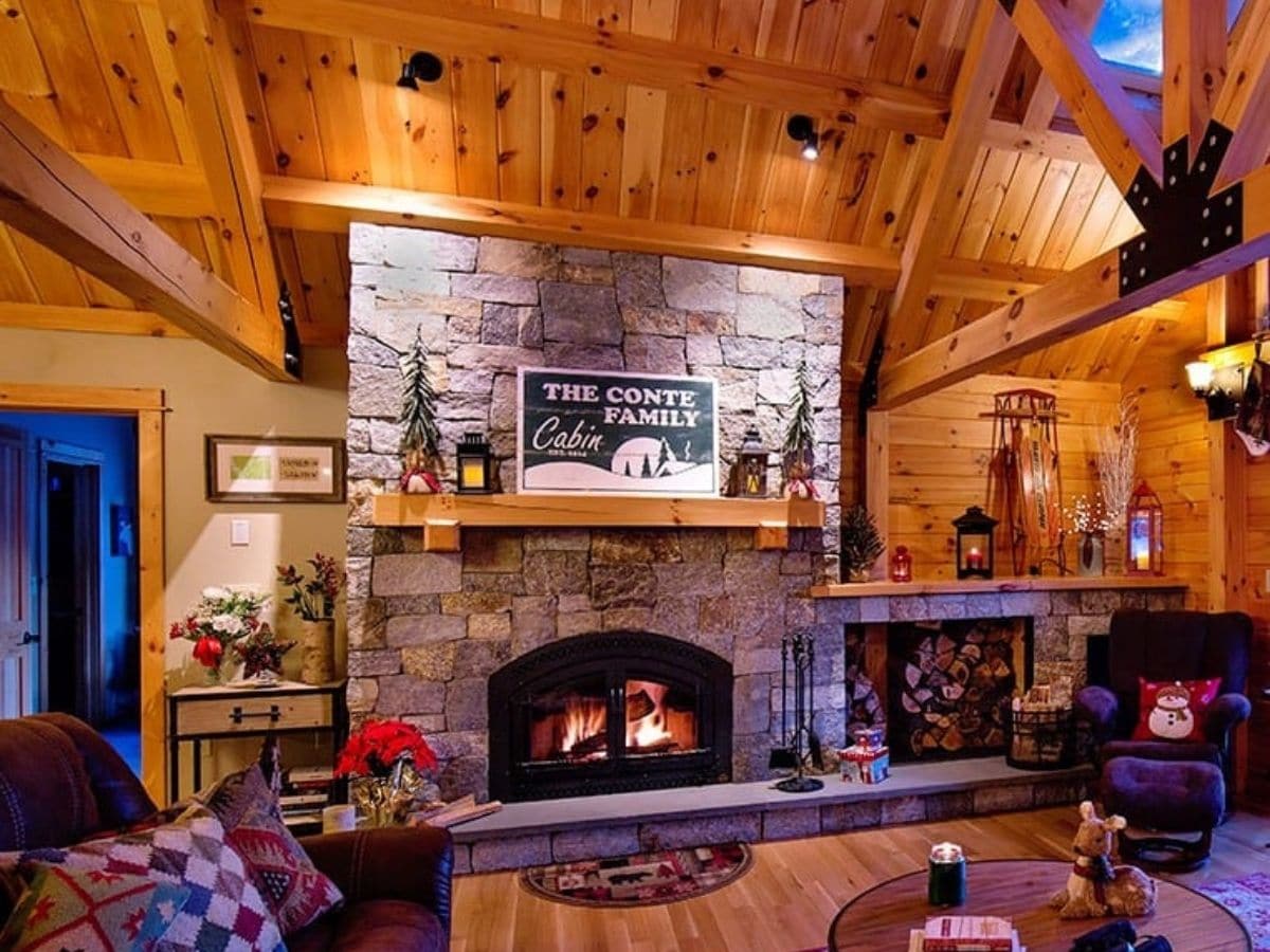 stone fireplace with wood mantle against wall below log ceiling with fire lit in fireplace