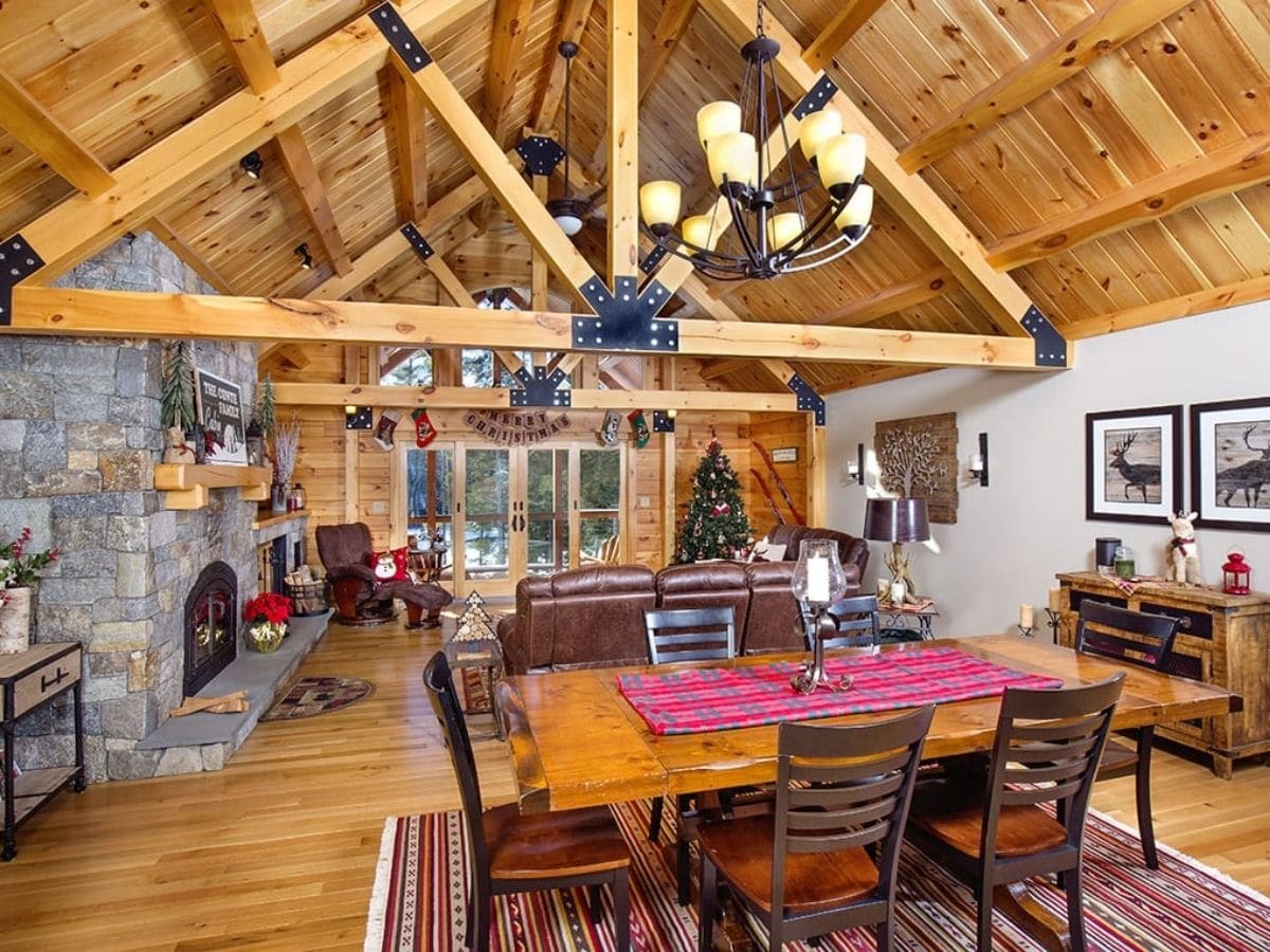 dining table in foreground with great room of log cabin in background and exposed beam trusses in middle of ceiling