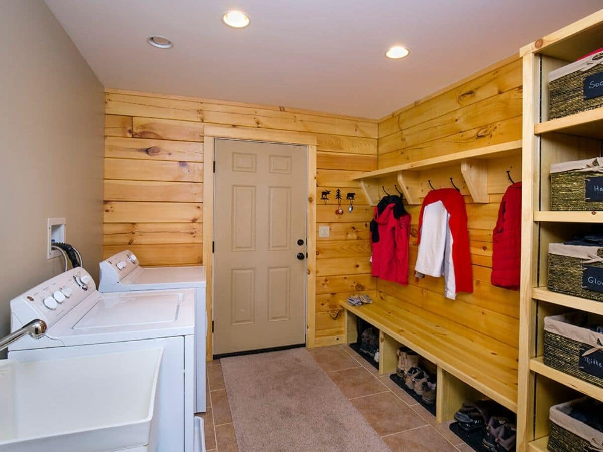 laundry room with hooks and shelves on right holding red jackets and white washer and dryer on left