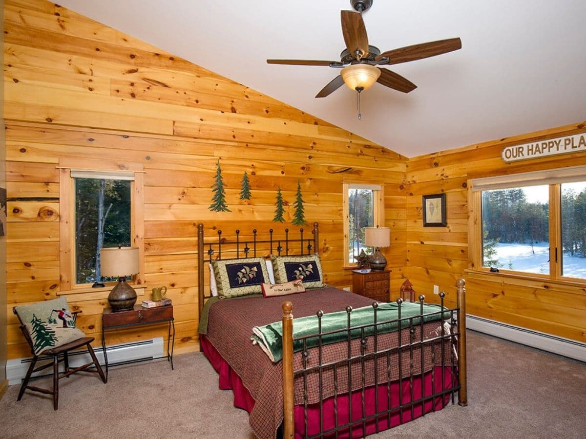 bedroom with wrought iron railing on footboard of bed with dark red blankets and ceiling fan above