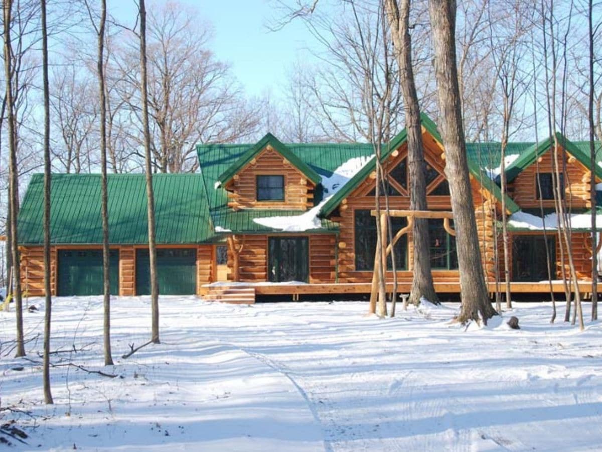 log cabin in snowy lot with trees in front 
